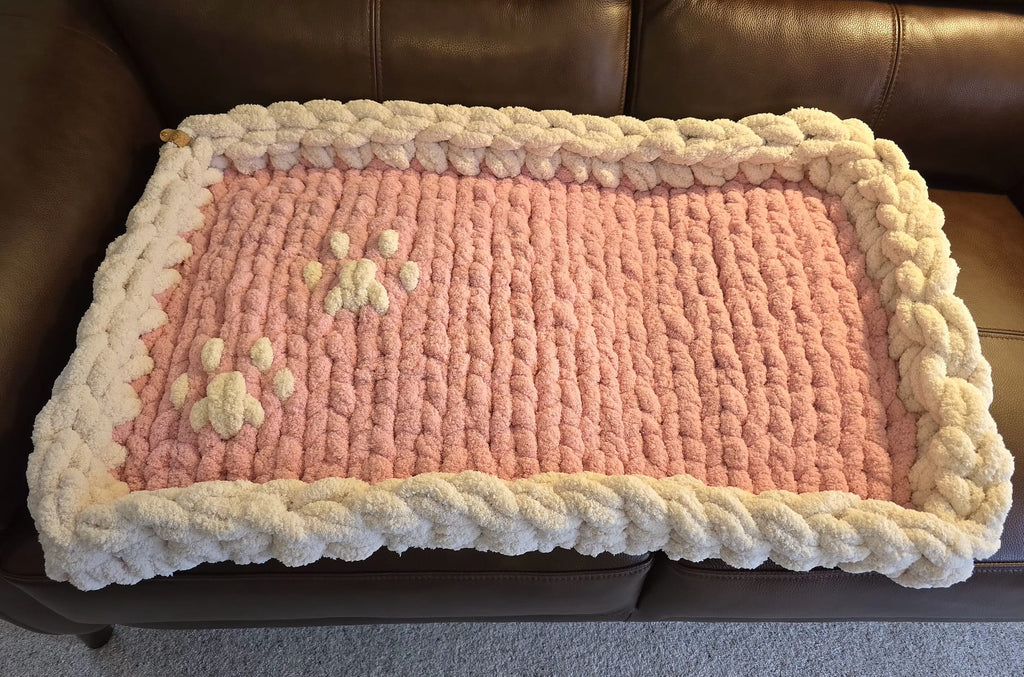 Pink knitted blanket with paw prints on a brown leather couch