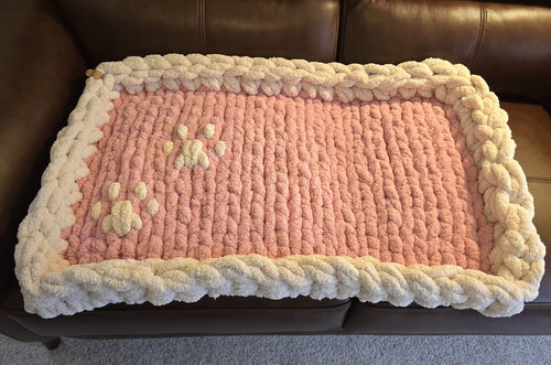 Pink knitted blanket with paw prints on a brown leather couch