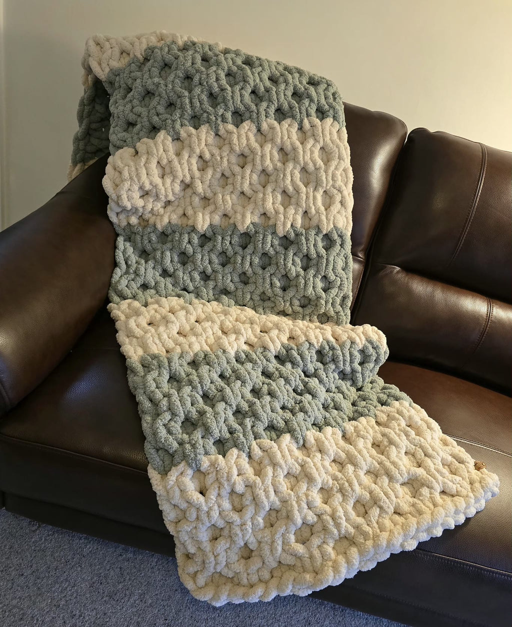 Knitted blanket in green and white draped over a brown leather couch.