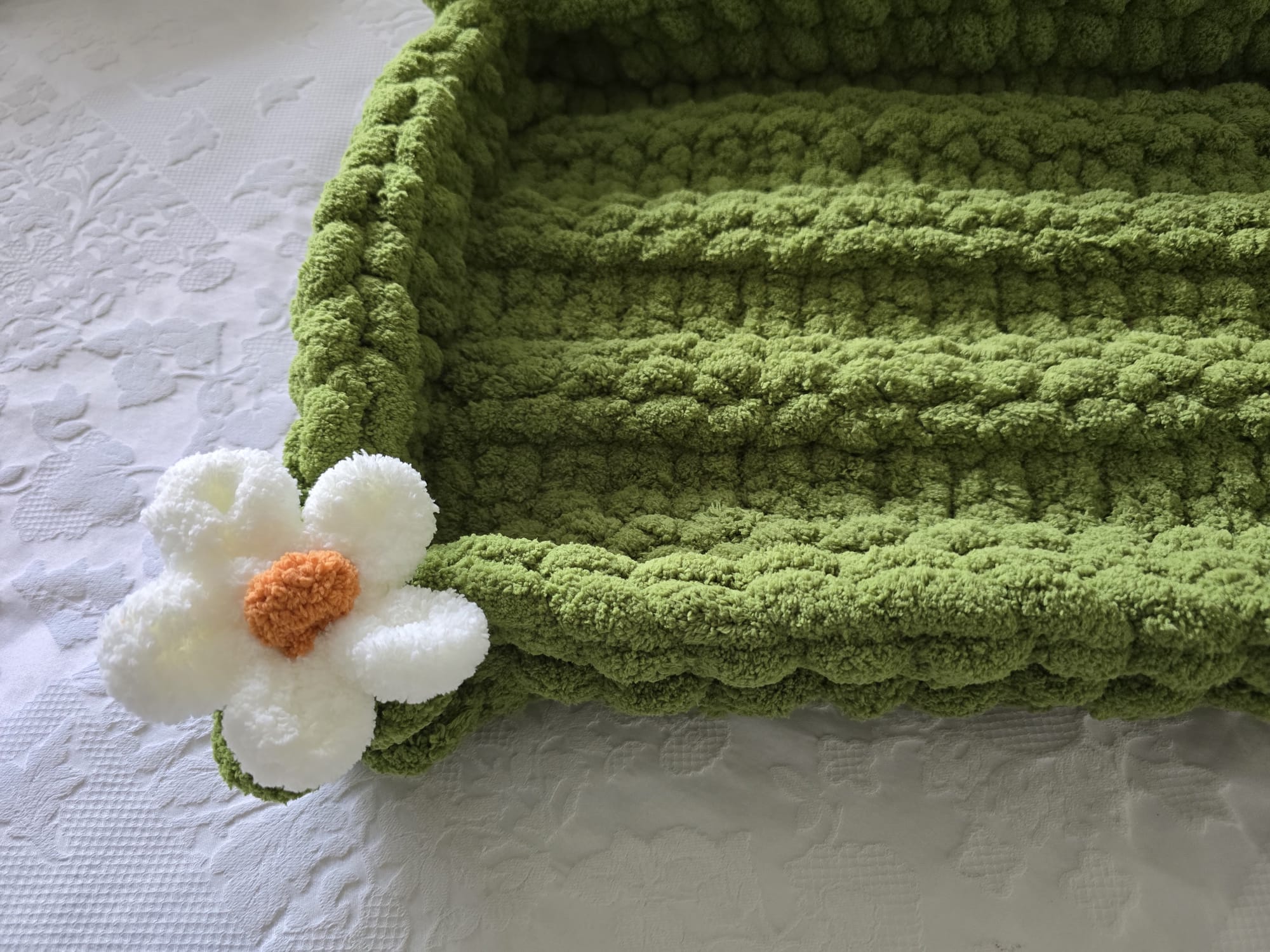 Green textured blanket with a white flower toy on a white surface
