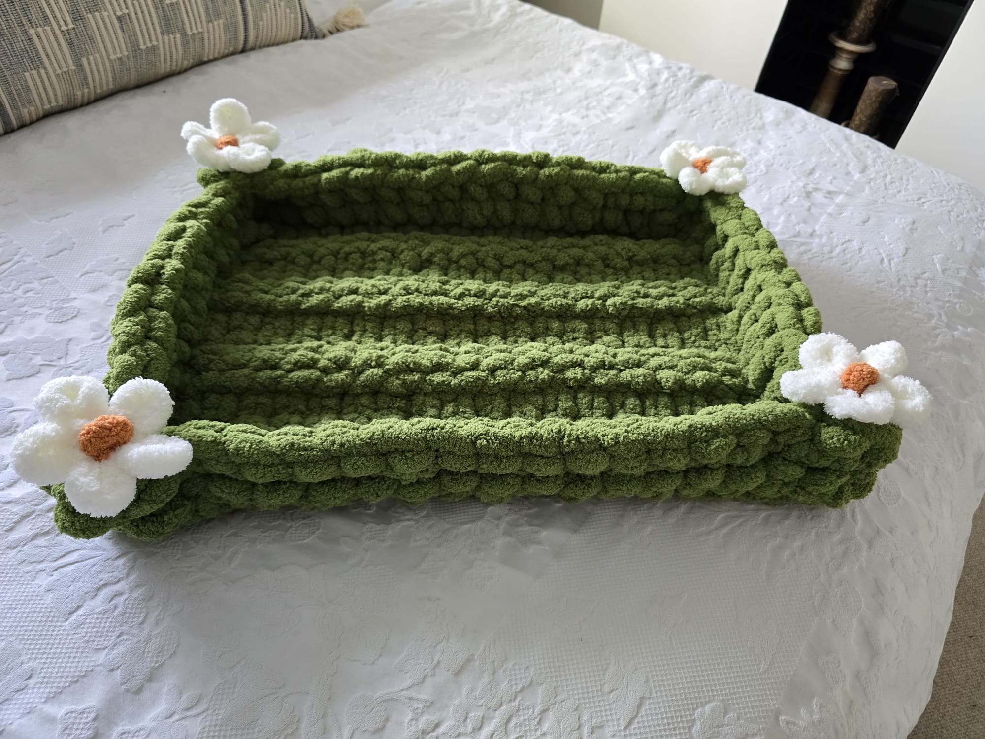 Green knitted pet bed with white flowers on a white surface