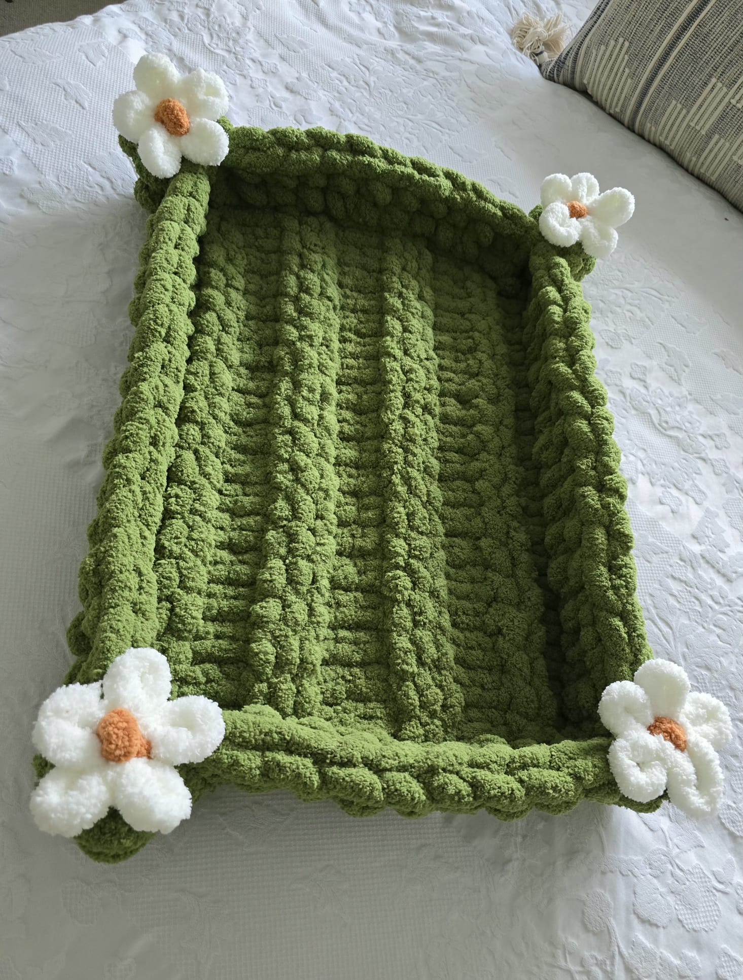 Green knitted pet bed with white floral decorations on a white surface
