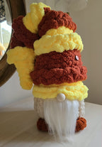 Crocheted gnome with a brown and yellow hat on a white surface